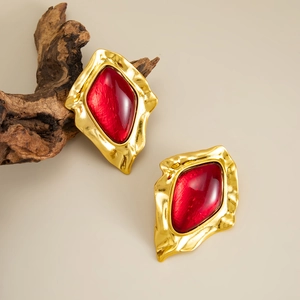 Detail of vintage gold earrings with irregular hammered texture and red resin gemstone