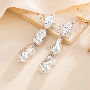 Detail of silver drop earrings with irregular molten metal beads on a beige stone stand
