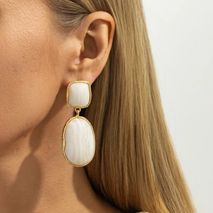 Close-up of geometric resin drop earrings featuring white stone inlay in gold-tone setting