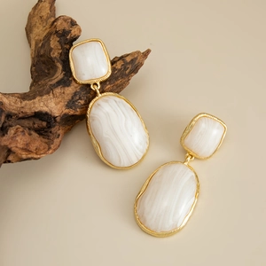 Detail view of geometric golden earrings with white marble resin on a beige pedestal