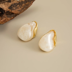 Close-up of cream marble resin earrings with wavy gold metal trim on a natural wood base
