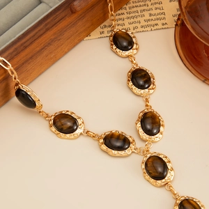 Macro detail of gold-tone Y-necklace featuring brown tiger eye stones and textured metal rims
