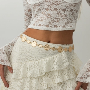 Close-up of golden metal waist chain with hammered texture circles on white lace skirt