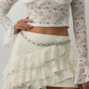Detail of silver irregular oval hollow waist chain on white lace fabric background