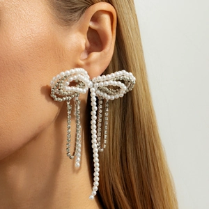 Faux pearl bow tassel earrings with sparkling rhinestones worn on a model's ear