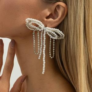 Elegant pearl bow earring with sparkling rhinestone tassels shown on a model