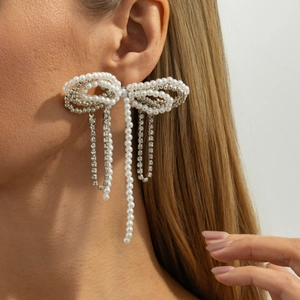 Detailed view of silver bow earrings with artificial pearls and shimmering tassels