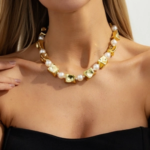 Detail van gouden geometrische metalen delen en witte parels op een korte ketting