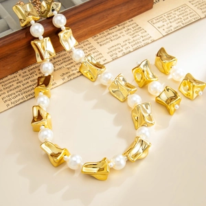 Detailopname van parelketting met goudkleurige geometrische kralen en oorbellen