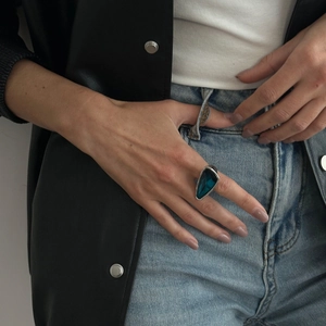 Detail of silver ring featuring a triangular blue crystal on model wearing leather jacket