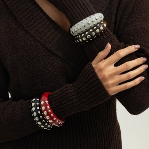 Detail of multi-colored punk bangles with silver studs worn over a brown knit sweater