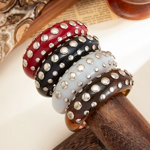 Detail of four punk style resin bangles with silver studs on a wooden display stand