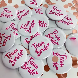 Close-up of white Team Bride badges with pink text for wedding party celebrations