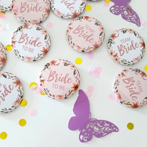 Flat lay of Bride To Be and Team Bride floral wedding tinplate badges with pink confetti