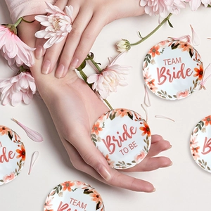 Close-up of floral Bride TO BE and TEAM Bride tinplate badges on a flower petal background