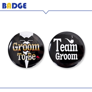 Dettaglio delle spille Groom To Be e Team Groom con grafica di smoking e pipa
