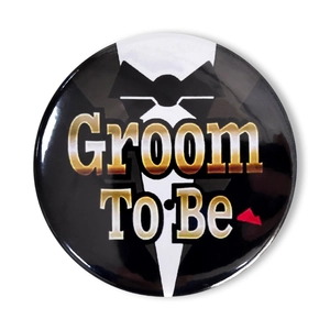 Dettaglio di una spilla rotonda Groom To Be con design smoking nero e scritte metalliche