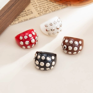 Flat lay of four colorful resin rings with silver studs in red, white, brown, and black