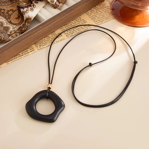 Detail of matte black irregular pendant with gold bead accent on long cord necklace
