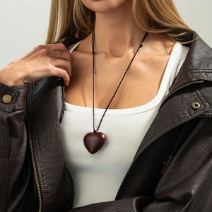 Detail view of a smooth dark wood heart pendant necklace on a stylish leather jacket