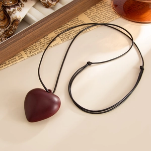 Detail of a matte deep red heart pendant necklace on vintage paper and wood background