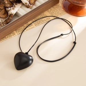 Detail view of a matte black heart pendant on an adjustable cord against a vintage background