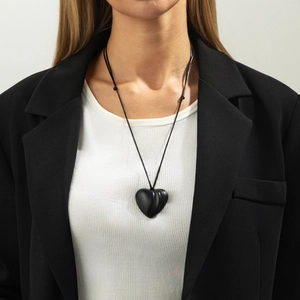 Close-up of a smooth black heart pendant on a simple cord worn over a white shirt