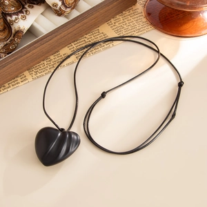 Close-up of textured black heart pendant on adjustable cord with vintage background