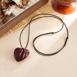 Close-up of heart-shaped wooden pendant with vertical textures on black cord