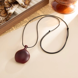Macro view of smooth deep-red wooden oval pendant with black braided adjustable rope