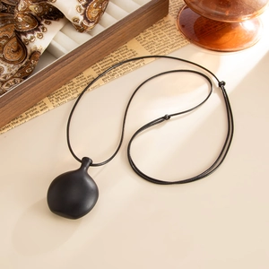 Detail of matte black pebble pendant on adjustable cord necklace over vintage background