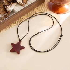 Detail shot of a reddish-brown wooden star pendant on an adjustable black cord necklace