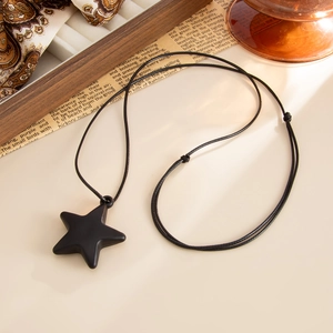 Detail of matte black star pendant with adjustable wax rope on a vintage aesthetic background