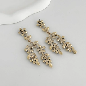 Détail des boucles d'oreilles vintage dorées avec fleurs et pompons de feuilles