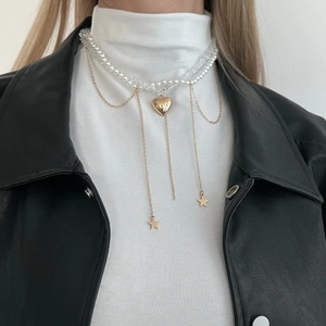 Detail of layered gold heart and star pendant necklace worn over a white turtleneck sweater