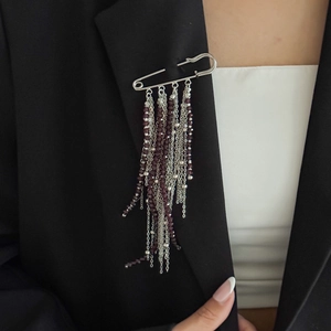 Detail of silver safety pin brooch with burgundy beads and layered fringe chains on suit