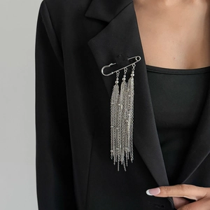 Dettaglio ravvicinato di una spilla a balia con nappe argentate su un blazer nero