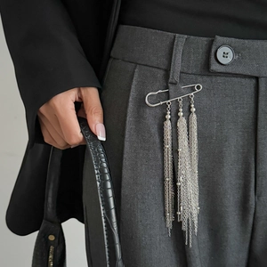 Silver safety pin brooch with metallic chain tassels on grey trousers detail
