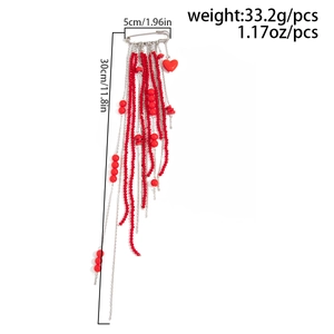 Detail of red bead tassel brooch with heart pendant and silver chains on white background