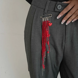 Detail of red bead tassel brooch with silver pin and heart pendant on dark suit fabric