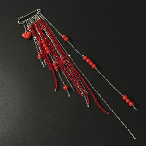 Detail of silver safety pin brooch with layered red bead tassels and heart charms