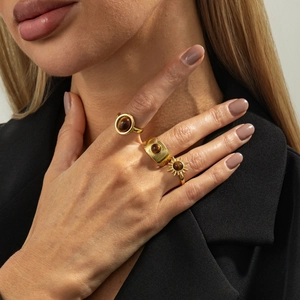 Detailansicht goldener Ring-Set mit braunem Edelstein und Sonnenstrahl-Textur an der Hand