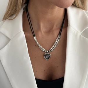 Detail einer Halskette mit Silberperlen und Schildanhänger an Model in weißem Blazer