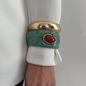 Gros plan sur un bracelet doré porté avec un jonc en résine verte orné d'une pierre