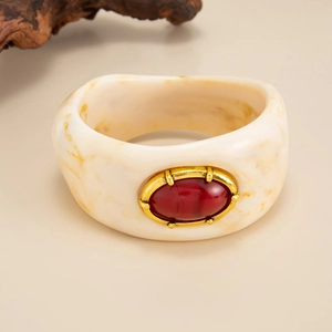 Détail du bracelet en résine marbrée avec pierre ovale rouge et bordure dorée