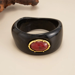Gros plan sur un bracelet en résine noire avec pierre rouge et bordure dorée
