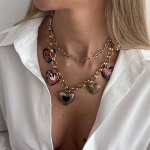 Detail of vintage layered gold chain with colorful enamel heart pendants on a white shirt