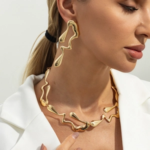 Détail d'une parure dorée abstraite en métal liquide portée sur un blazer blanc