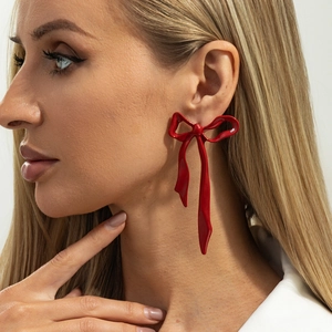 Close-up of a model wearing a shiny red ribbon bow earring with a polished enamel finish