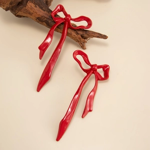 Detailed view of oversized red bow earrings with glossy finish and wavy ribbon texture